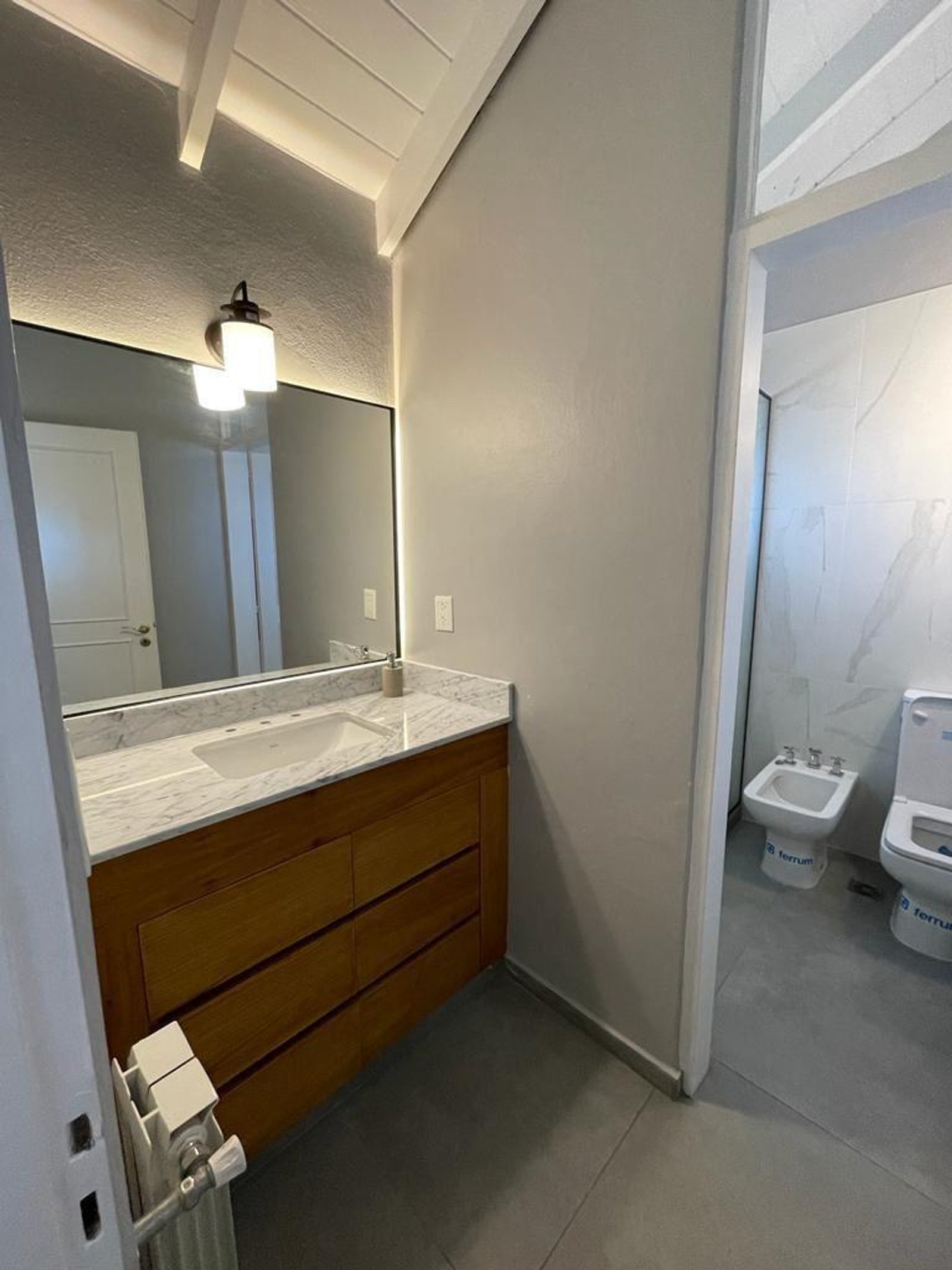 Baño moderno con vanitory de madera, bacha integrada y luz cálida — proyecto Acassuso, por Estudio NET Arquitectura , en Domingo de Acassuso